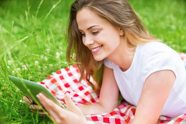 Junge Frau mit Tablet im Freien auf Gras liegend, lächelnd — Stockfoto