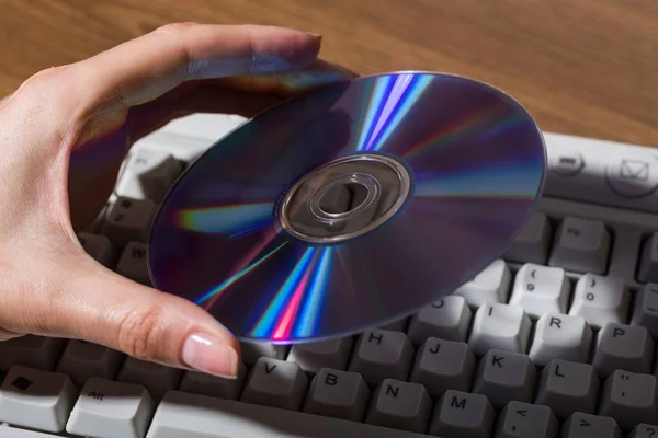 Hand hält CD / DVD auf Computertastatur — Stockfoto