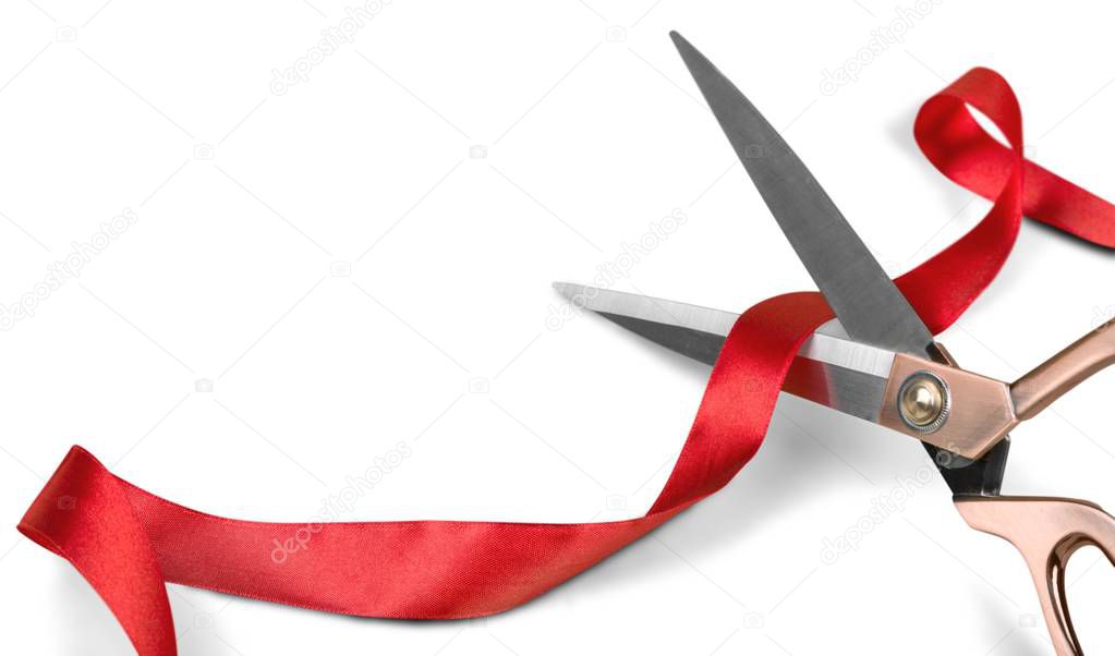 Scissors cutting red ribbon, close-up view on background