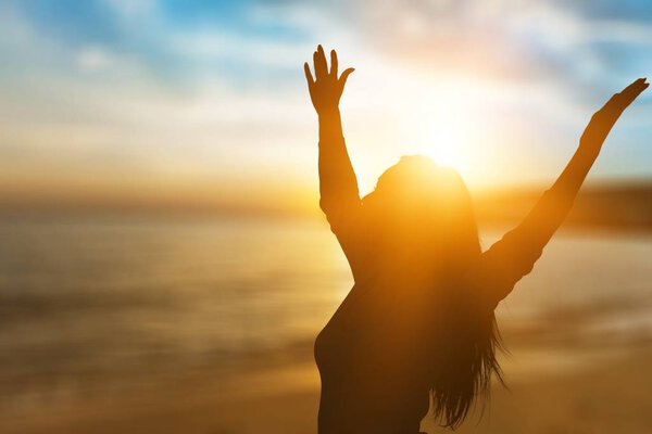 Woman with raised hands at sunset