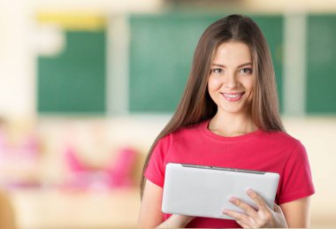 Üniversitede elinde tablet olan gülümseyen genç bir kadın.