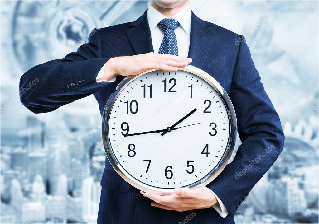 Portrait of young business man holding clock on blurred background 
