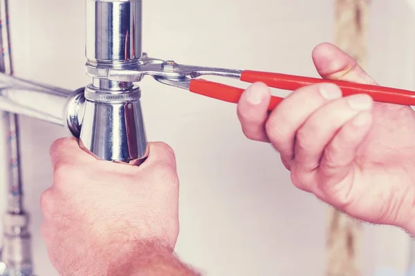 Handen van een loodgieter met wastafel en moersleutel. — Stockfoto