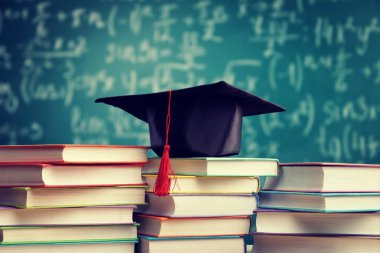 Mezuniyet şapka ve ahşap masa üzerinde kitap yığını