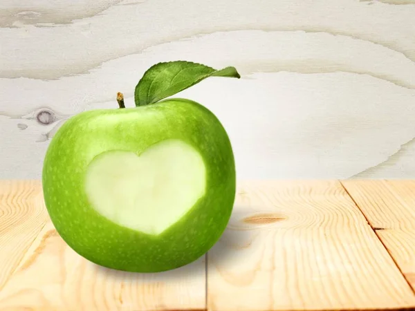 Apple with carved heart sign on wooden table