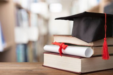 Mezuniyet şapka ve ahşap masa üzerinde kitap yığını