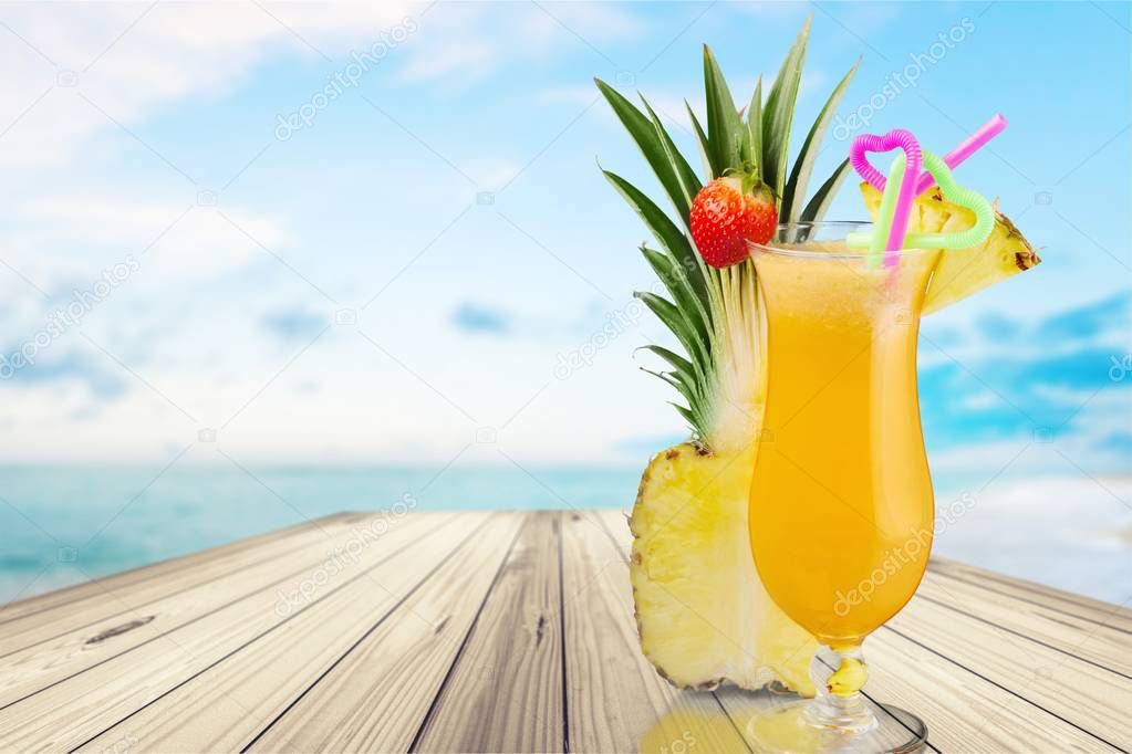 Glass with alcohol cocktail and pineapple on sandy beach