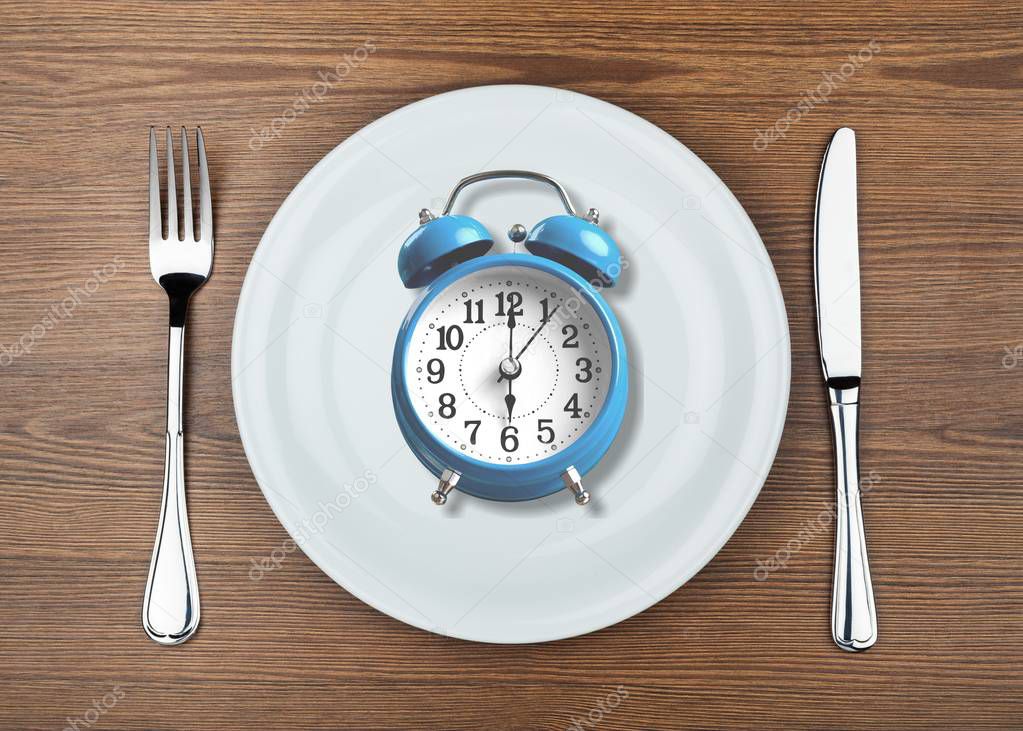 alarm clock on plate on wooden background 