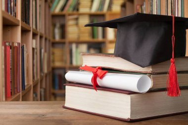 Mezuniyet şapka ve ahşap masa üzerinde kitap yığını