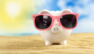 Kumlu plajda güneş gözlüğü ile Piggy banka 