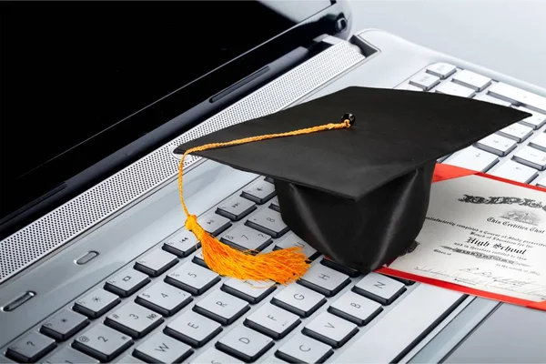 Laptop and diploma scroll and graduation hat