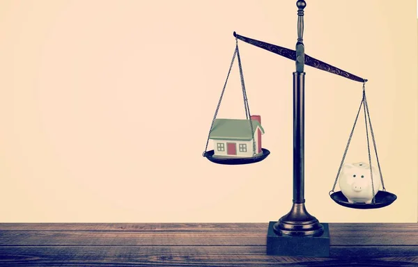 Law scales on table with house and piggy bank on it