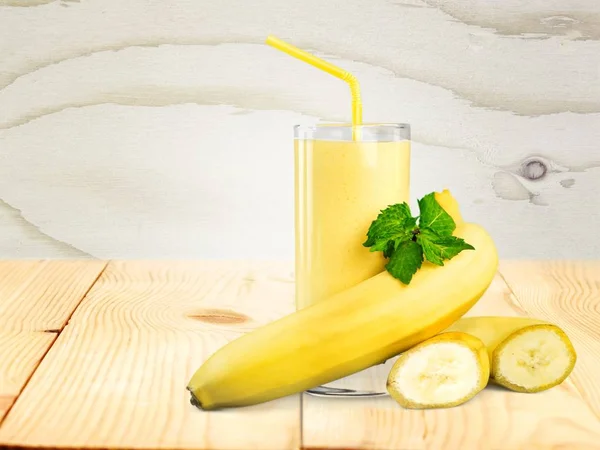 tasty banana juice in glass and raw bananas on wooden table