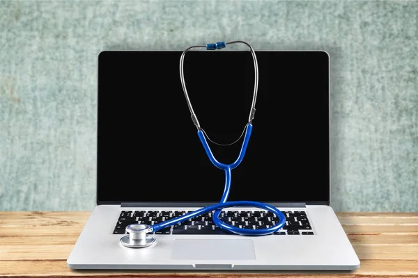 Modern laptop and stethoscope on background, close-up view