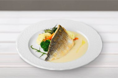 Beyaz tabakta sebzeli ızgara balık.