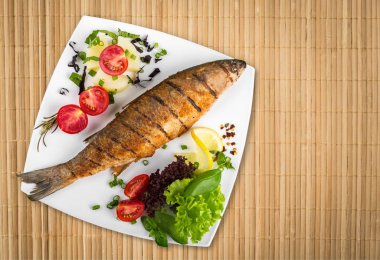 Beyaz tabakta sebzeli ızgara balık.