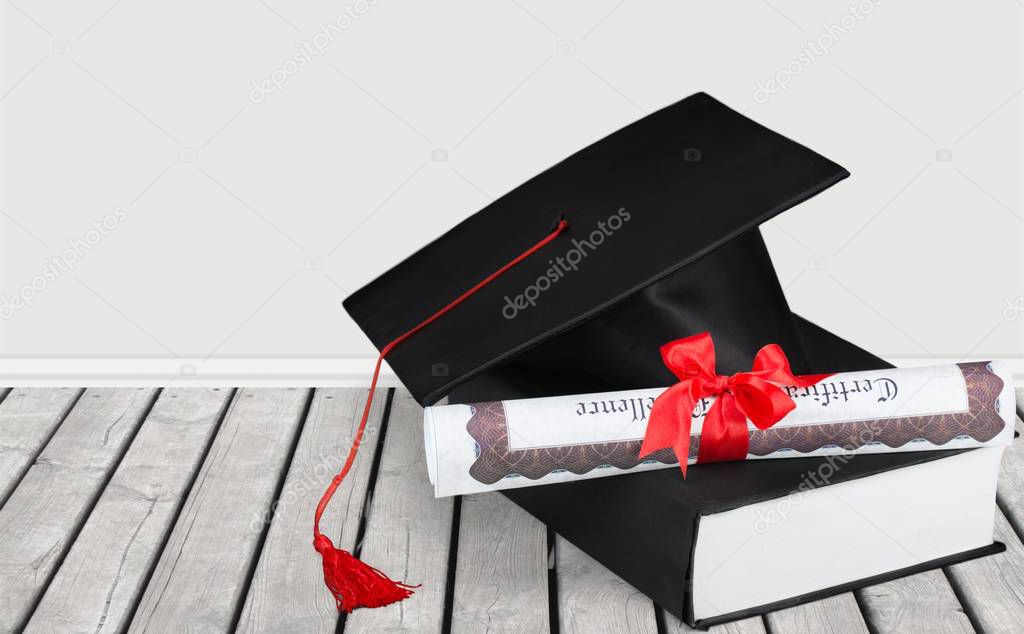 Graduation hat, book and diploma on wooden table