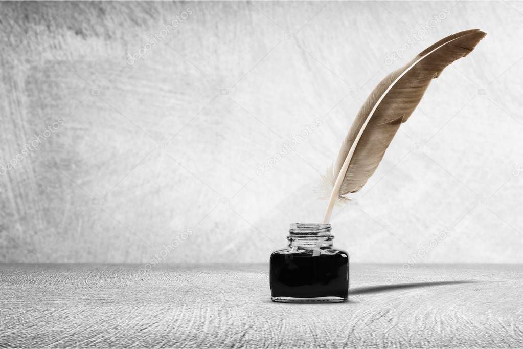 Feather quill pen and glass inkwell on background