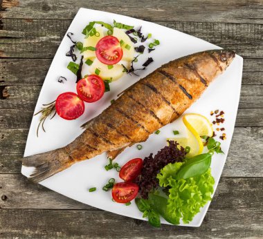 Beyaz tabakta sebzeli ızgara balık.