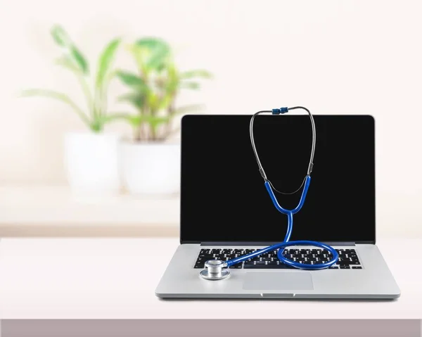 Modern laptop and stethoscope on background, close-up view