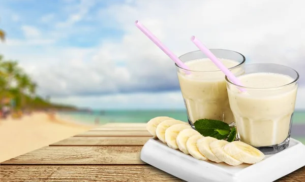 tasty banana juice in glass and raw banana on wooden table