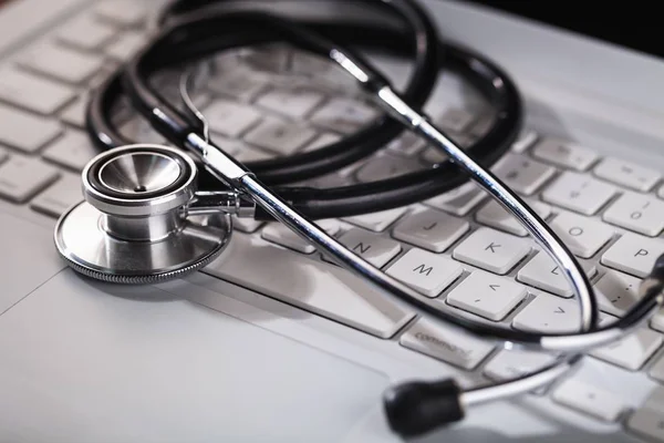 Modern laptop and stethoscope on background, close-up view