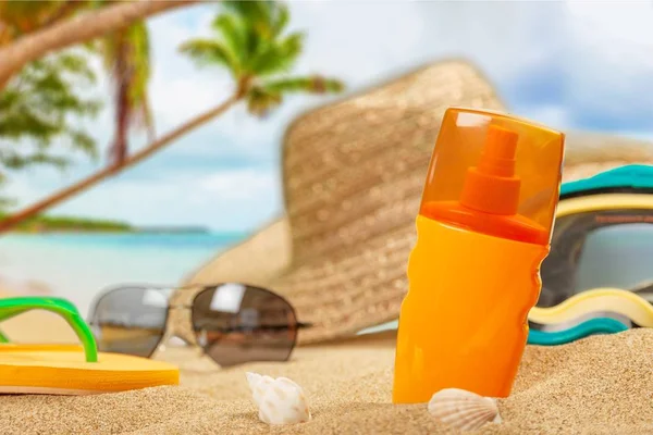 Bottle of sunscreen lotion,hat and shells on beach background