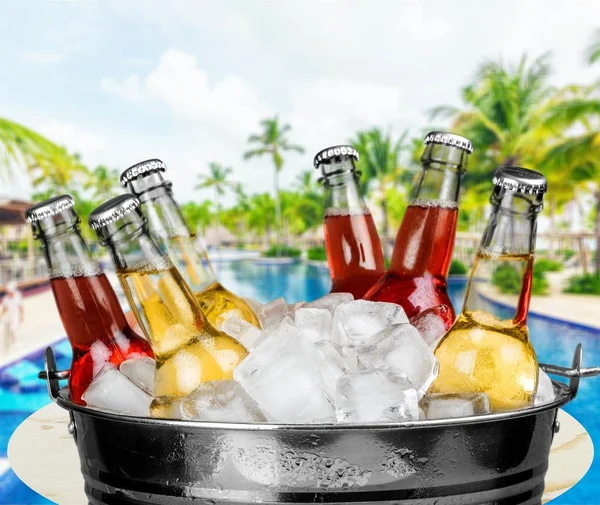 Beer bottles with ice in bucket on blurred background