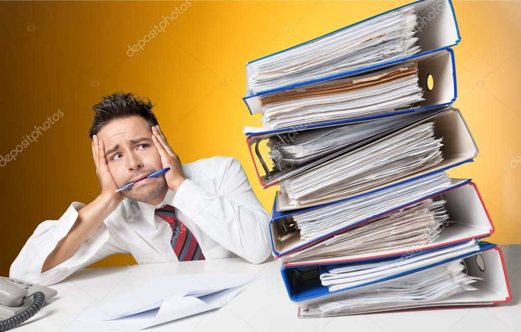 Tired businessman at office with pile of documents 