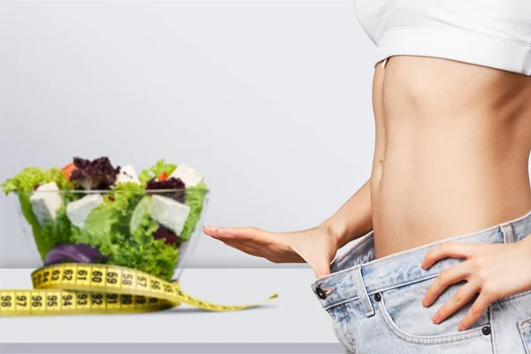 Young fit woman, healthy food and tape measure on background