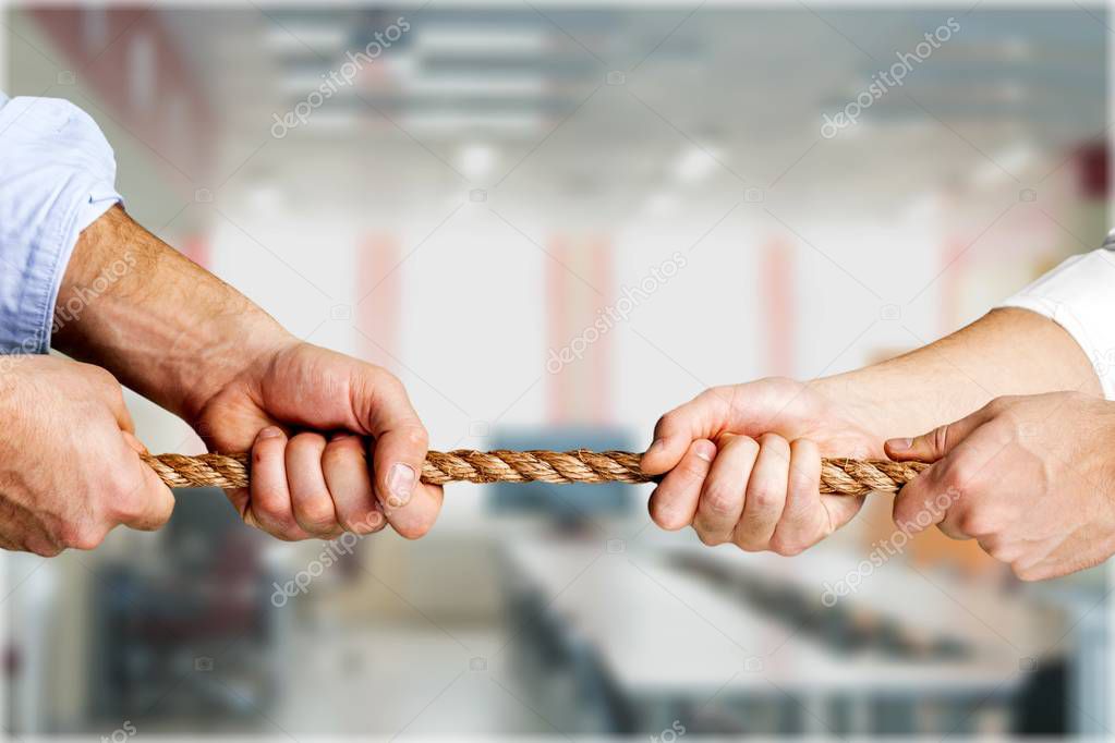 business people pulling rope in opposite directions at office
