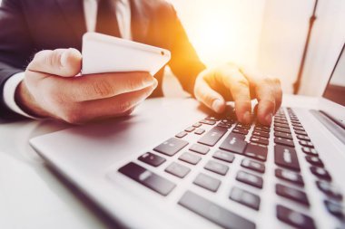 Arka planda telefonu ve bilgisayarı olan iş adamı 