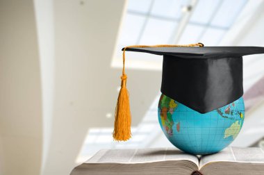 Mezuniyet şapkası, kitap ve diploma masada.