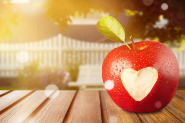 Tahta masaya oyulmuş kalp işareti ile taze olgun elma.
