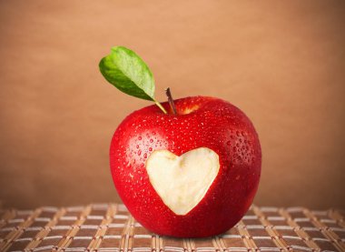 Taze olgun elma, masada oyulmuş kalp işareti var.