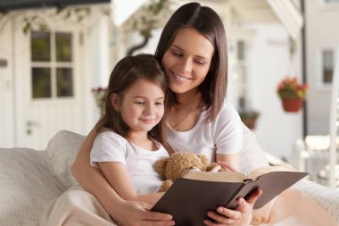 Anne ve kızı evde kitap okuyorlar.