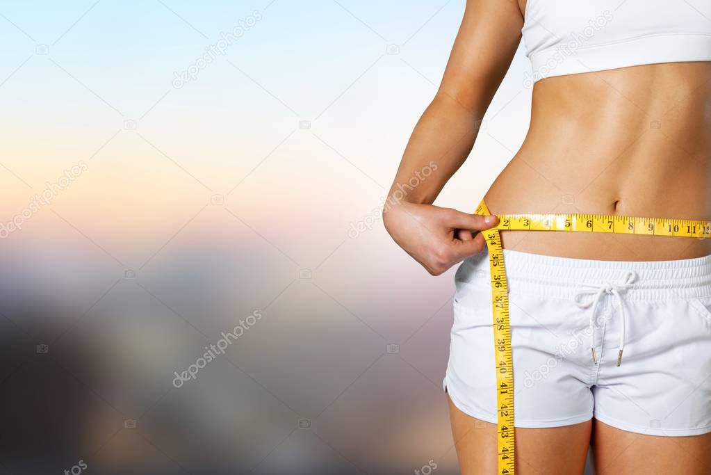Young woman measuring her waist on background