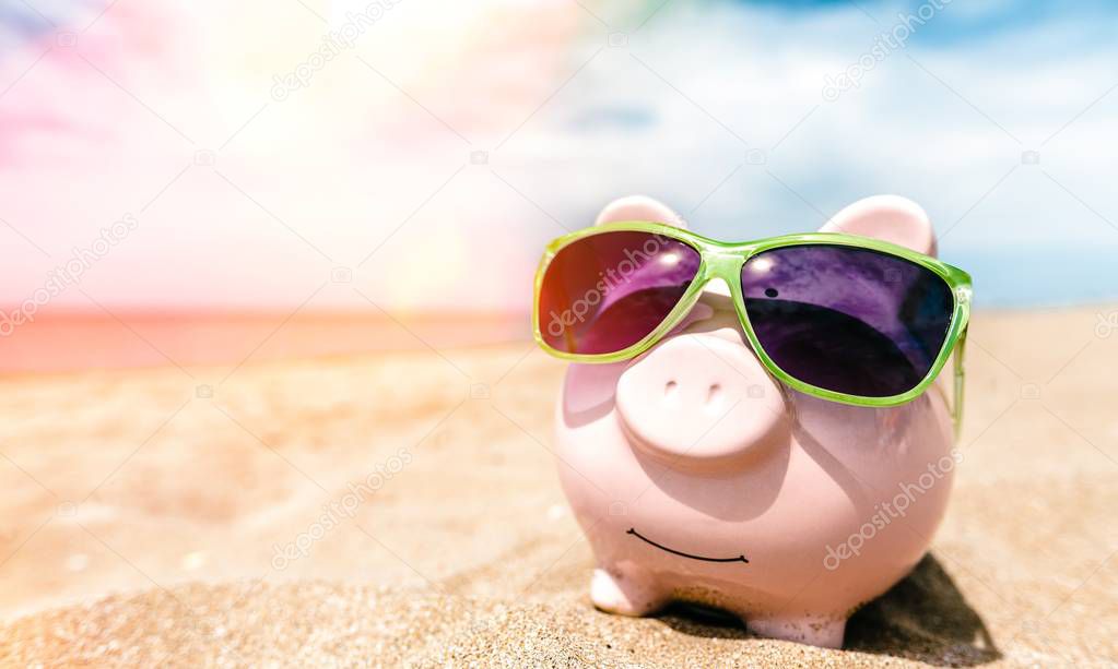 Summer piggy bank with sunglasses on the beach  