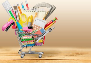 school supplies and tools in shopping cart on wooden background