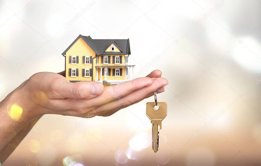 Hand holding house model and key on background 