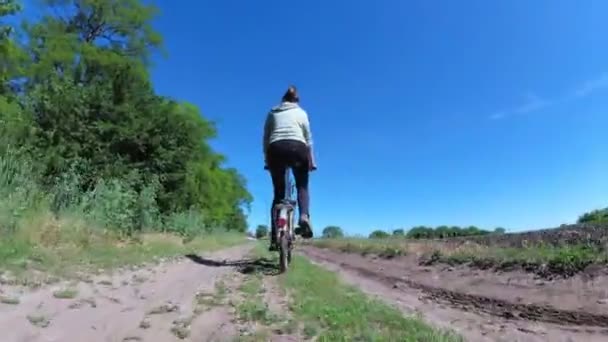Νεαρή γυναίκα ιππασία εκλεκτής ποιότητας ποδηλάτων κατά μήκος ενός αγροτικού δρόμου σε ένα χωριό — Αρχείο Βίντεο