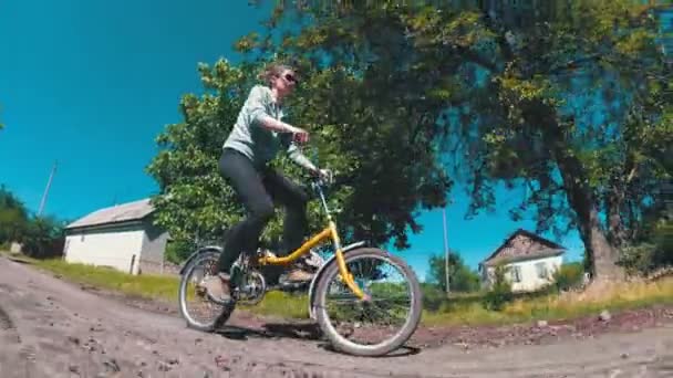 Jovem mulher andando de bicicleta vintage ao longo de uma estrada rural em uma aldeia — Vídeo de Stock