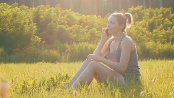 Boldog fiatal nő ül a zöld gyep, és a telefon vagy Smartphone beszélő — Stock videók