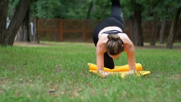 Junge Sportlerin in Sportkleidung praktiziert Yoga liegend auf einem Teppich in einem Park auf einem grünen Rasen — Stockvideo