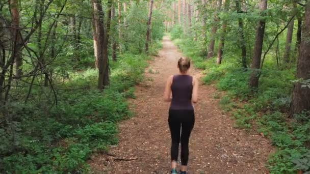 Вид с воздуха на молодую женщину, бегущую по тропе в густом сосновом лесу — стоковое видео
