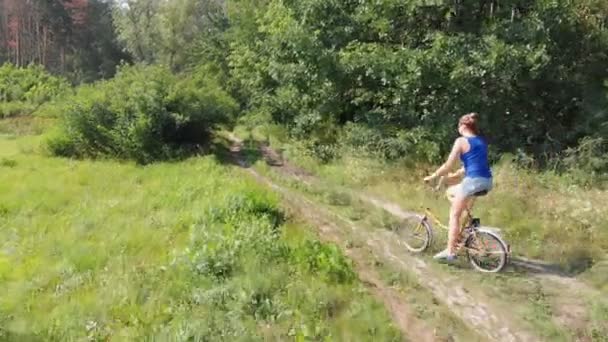 Flygfoto på flickan rider en Retro cykel på en grusväg i ett fält nära skogen. — Stockvideo