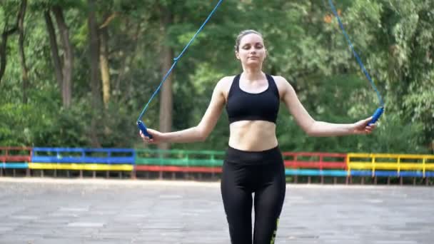 Mujer atleta joven en traje deportivo cómodo saltar la cuerda en un campo de deportes en el parque — Vídeos de Stock