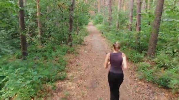 Flygfoto från baksidan till den unga kvinnan som löper längs sökvägen i en tjock tallskog — Stockvideo