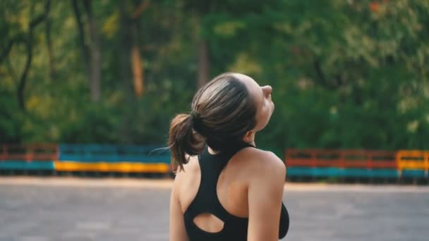 Молодая спортсменка в спортивном костюме делает шею на спортивном поле в парке — стоковое видео
