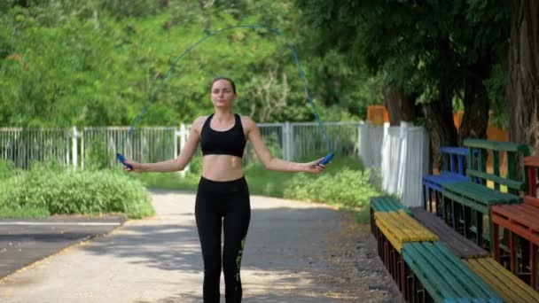Jeune athlète femme en tenue de sport confortable corde de saut sur un terrain de sport dans le parc — Video